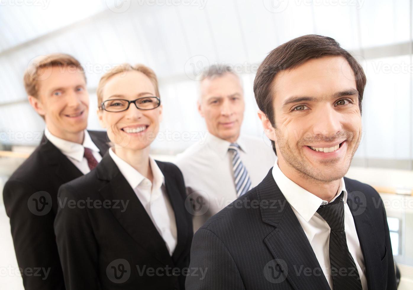 Successful team. Cheerful young man in formalwear looking at camera and smiling while his colleagues standing behind him photo