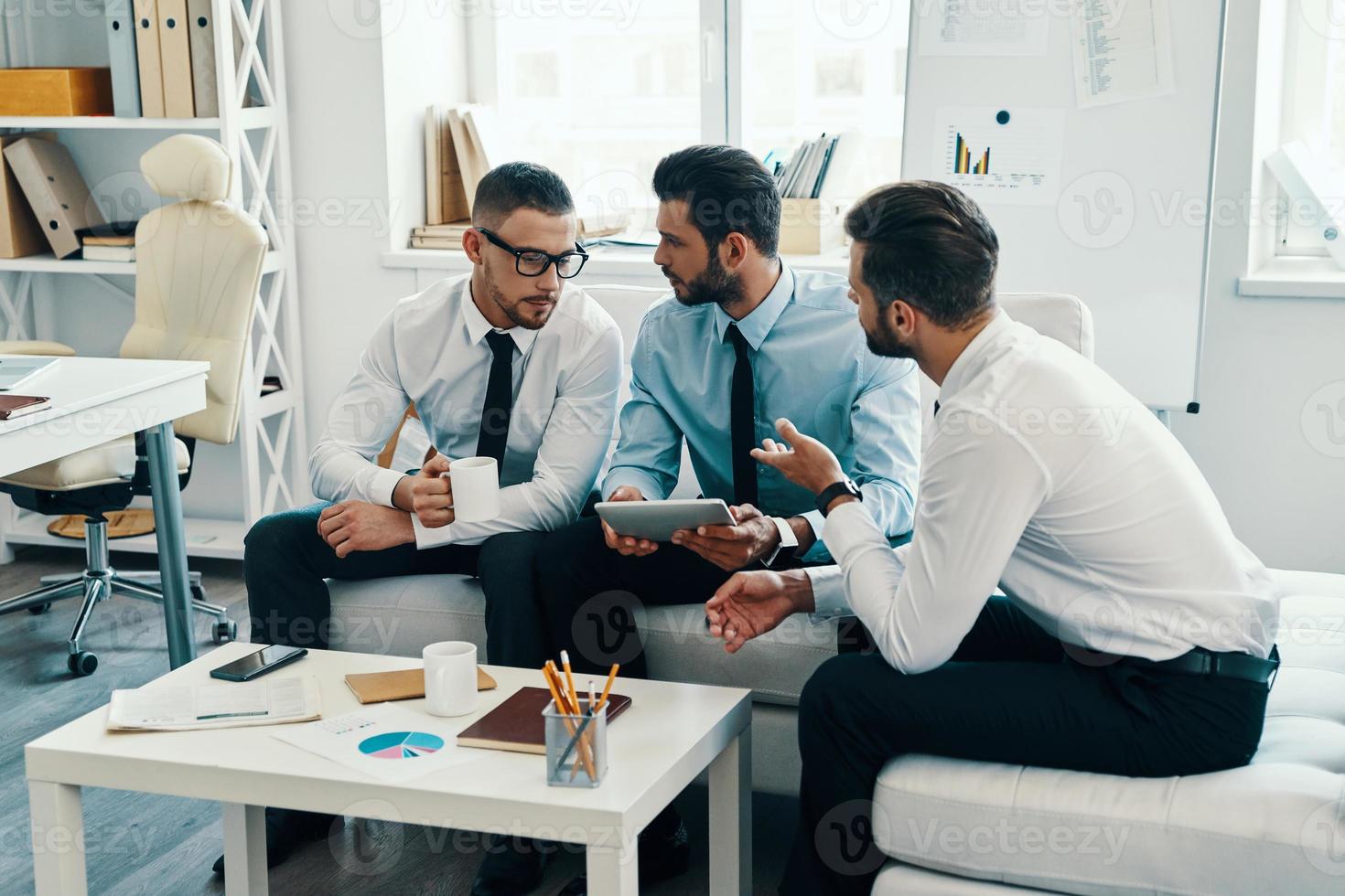 Confident and successful team. Group of young modern men in formalwear working using digital tablet while sitting in the office photo