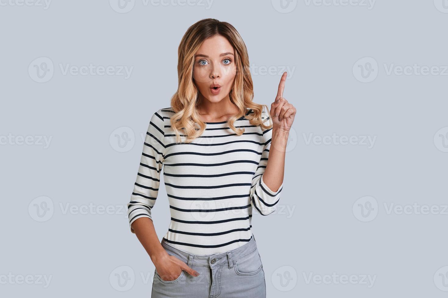 Idea Attractive young woman looking at camera and pointing copy space while standing against grey background photo
