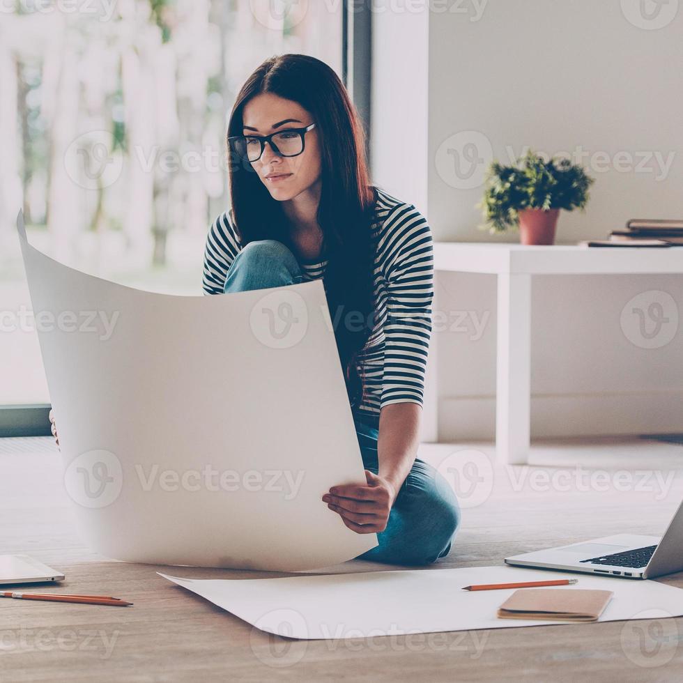 Examining blueprint. Confident young beautiful woman examining blueprint while sitting on the floor at home photo