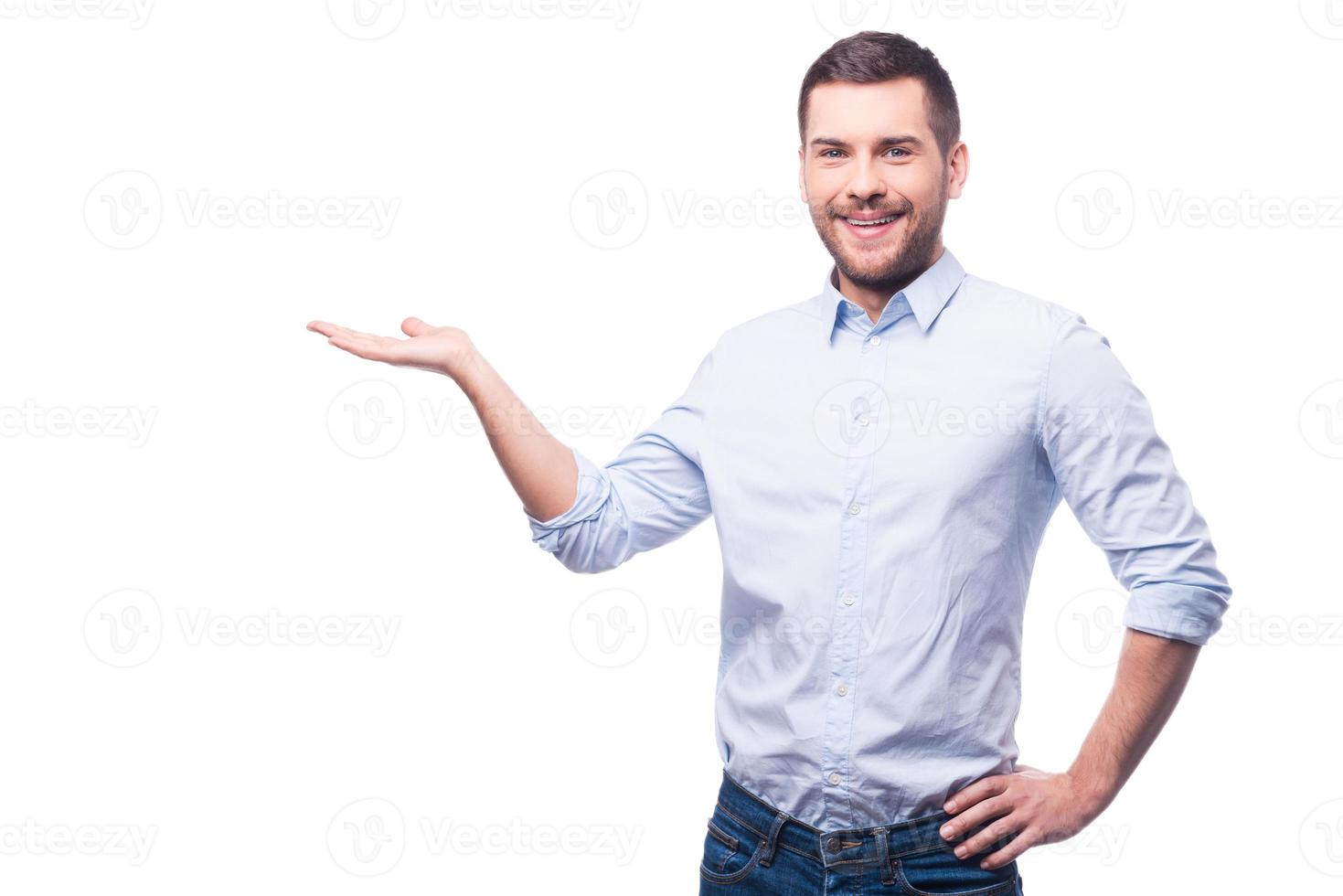 Presenting new project. Handsome young man in shirt looking at camera and holding copy space while standing against white background photo