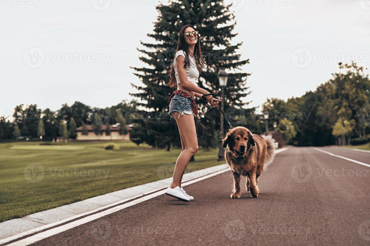 Full length of beautiful young woman playing with her dog and smiling while spending time outdoors photo