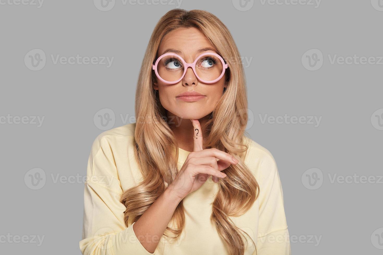 Searching for inspiration. Confused young woman looking away and gesturing while standing against grey background photo