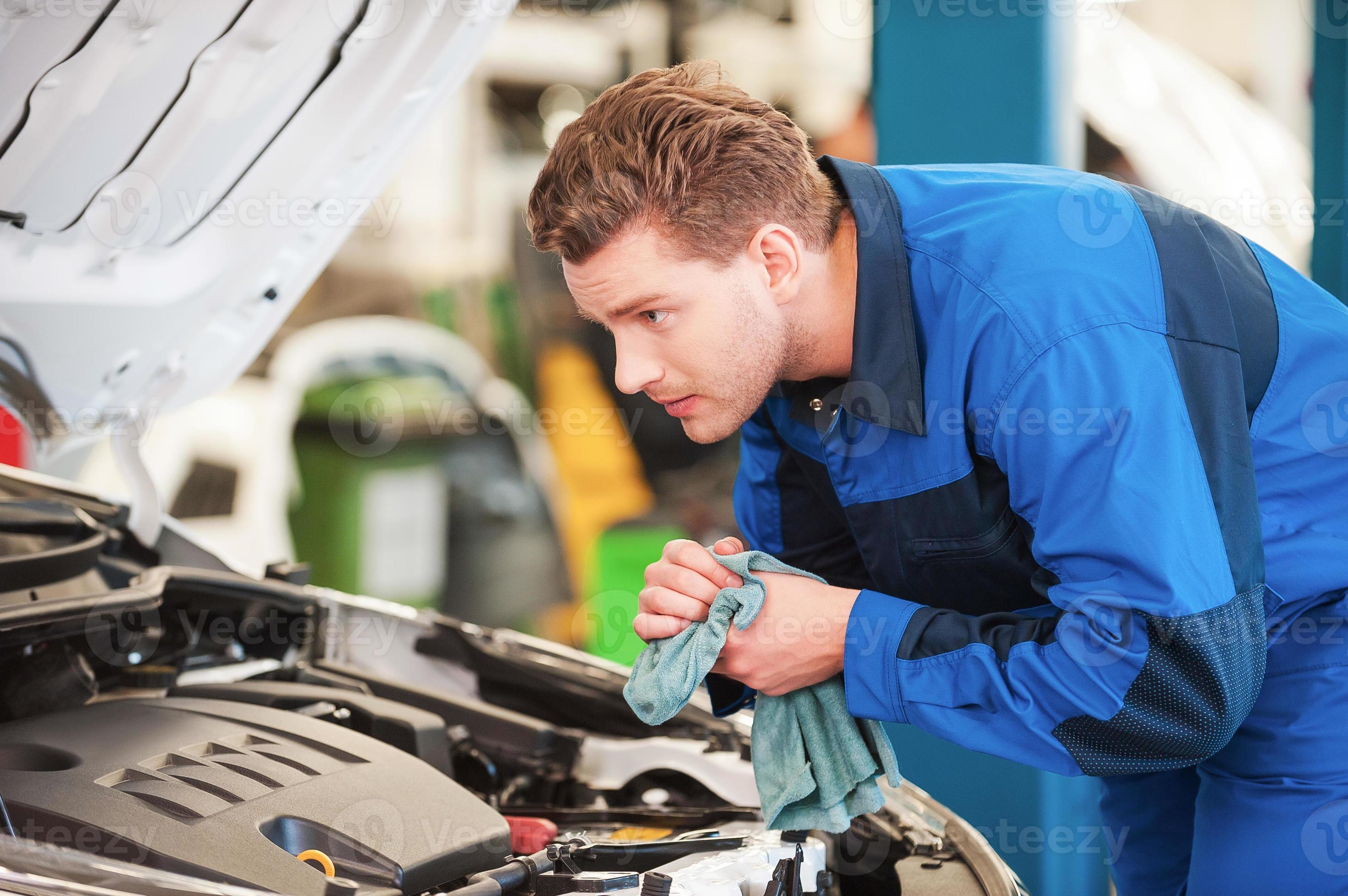 Mechanic at work. Concentrated young man in uniform examining car and