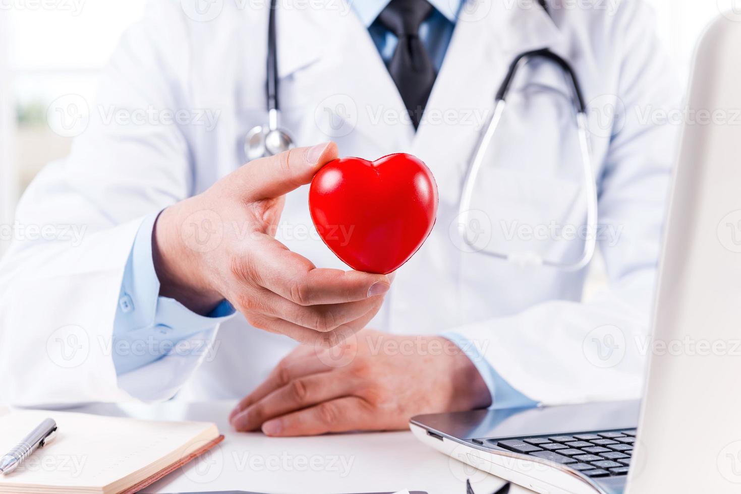 cuidando bien tu corazón. primer plano de un médico sosteniendo un juguete con forma de corazón mientras está sentado en su lugar de trabajo foto