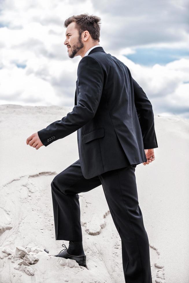 The only way is up. Side view of young businessman rising up by desert dune photo