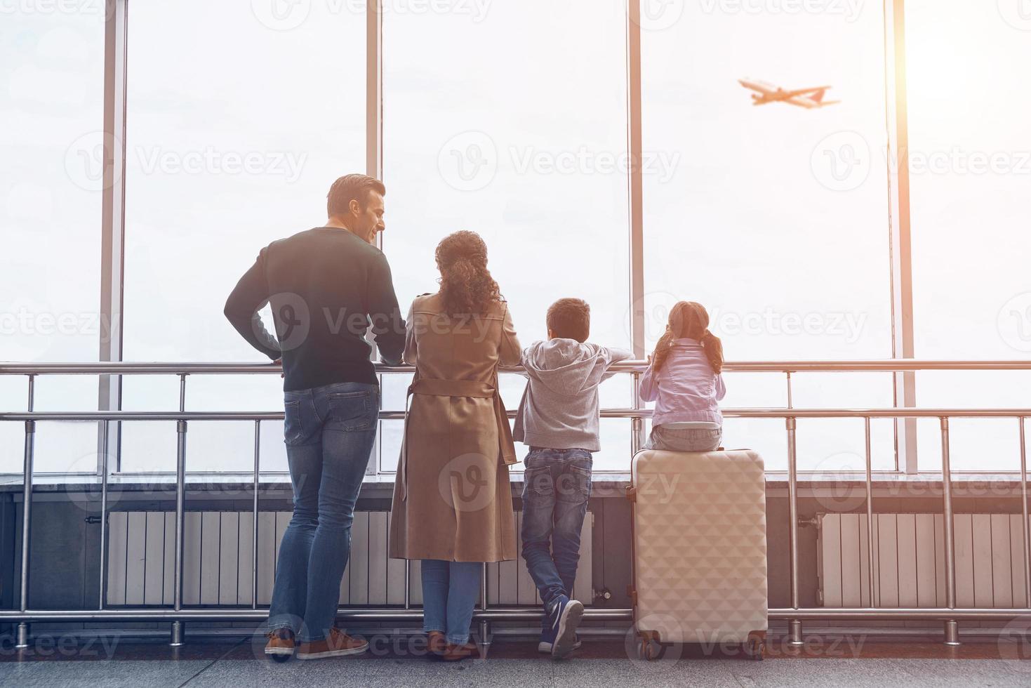 Full length of family with two little kids looking at the flying airplane while standing in airport terminal photo