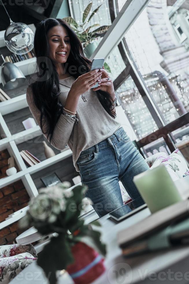 Receiving nice messages. Attractive young smiling woman holding smart phone and looking at it while standing in restaurant photo