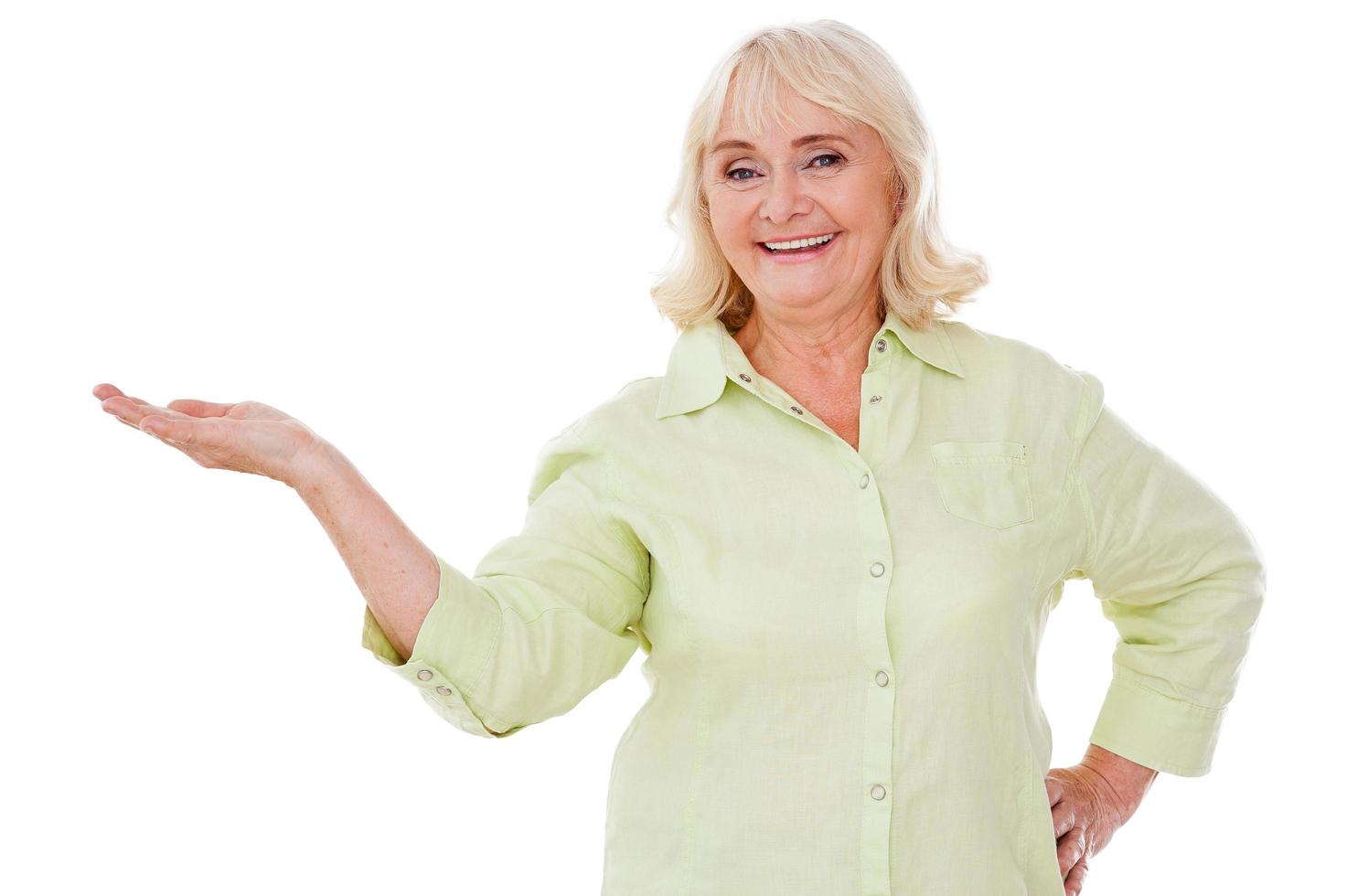 Copy space in her hand. Cheerful senior woman holding copy space and smiling while standing isolated on white background photo