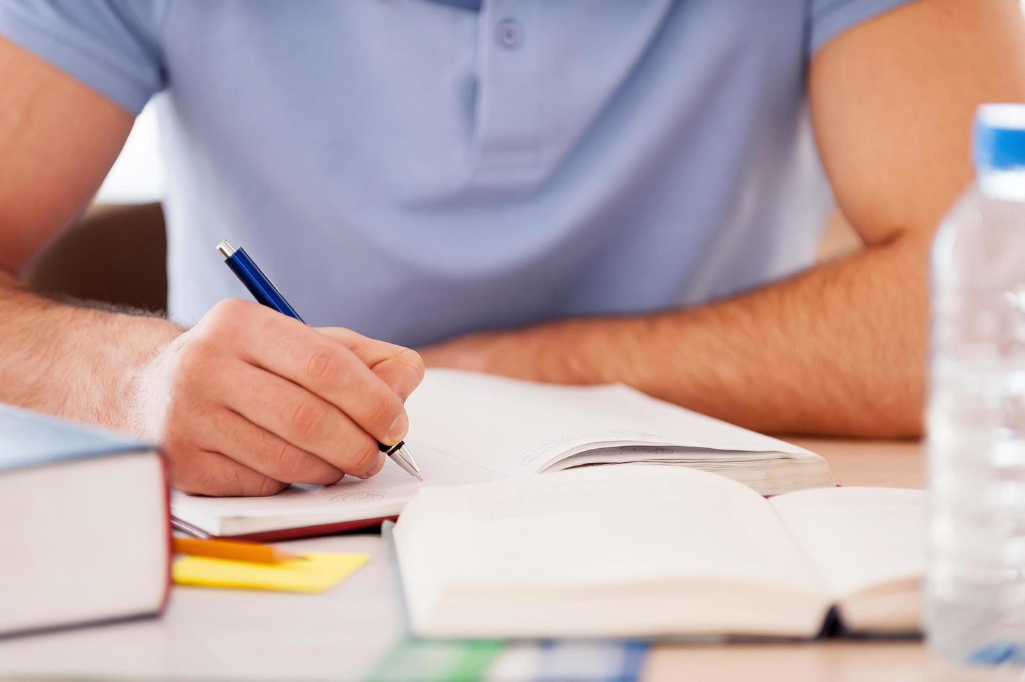 estudiando duro. imagen recortada de un estudiante escribiendo algo en un bloc de notas mientras está sentado en el escritorio foto