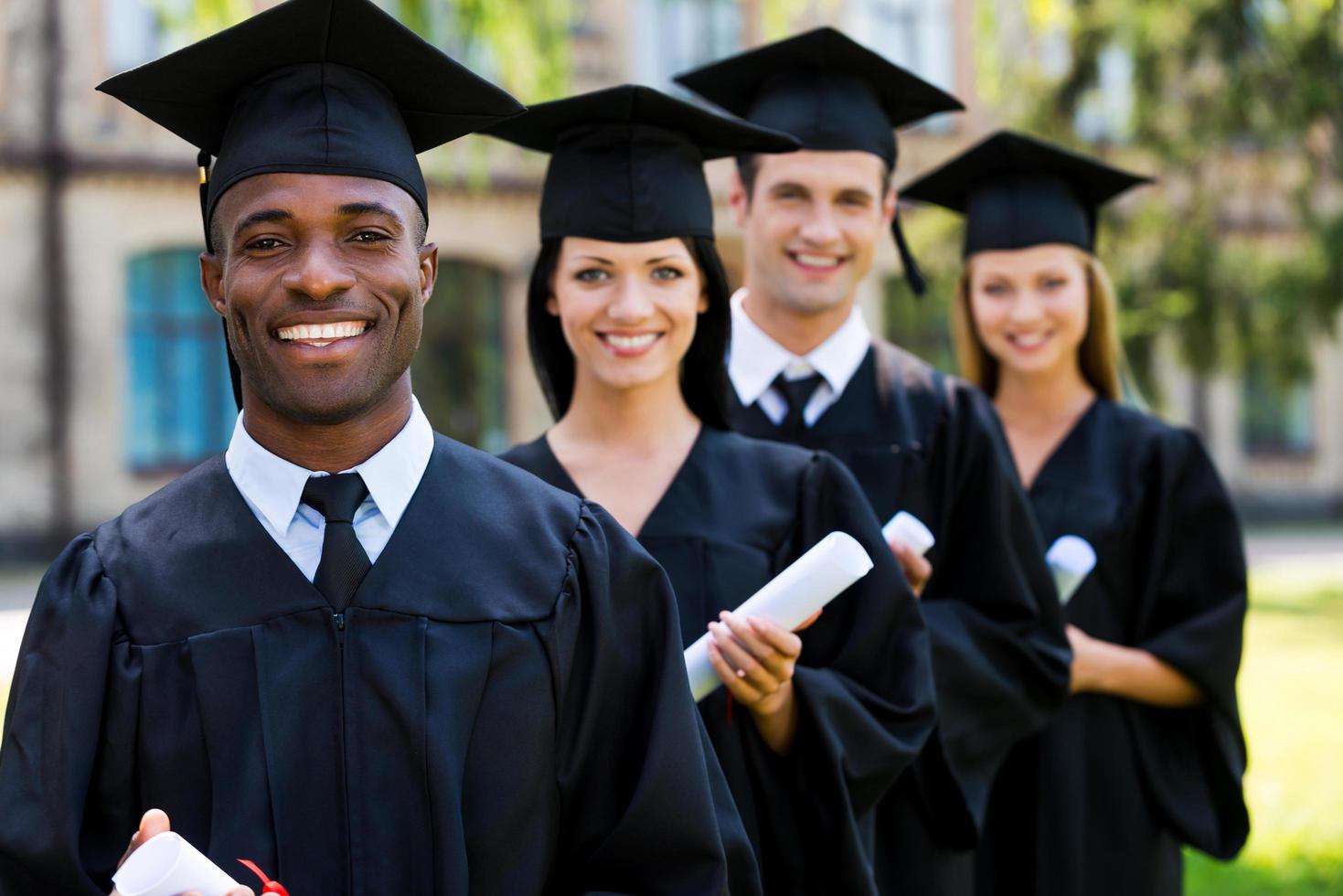 Happy college graduates. Four college graduates standing in a row and smiling photo