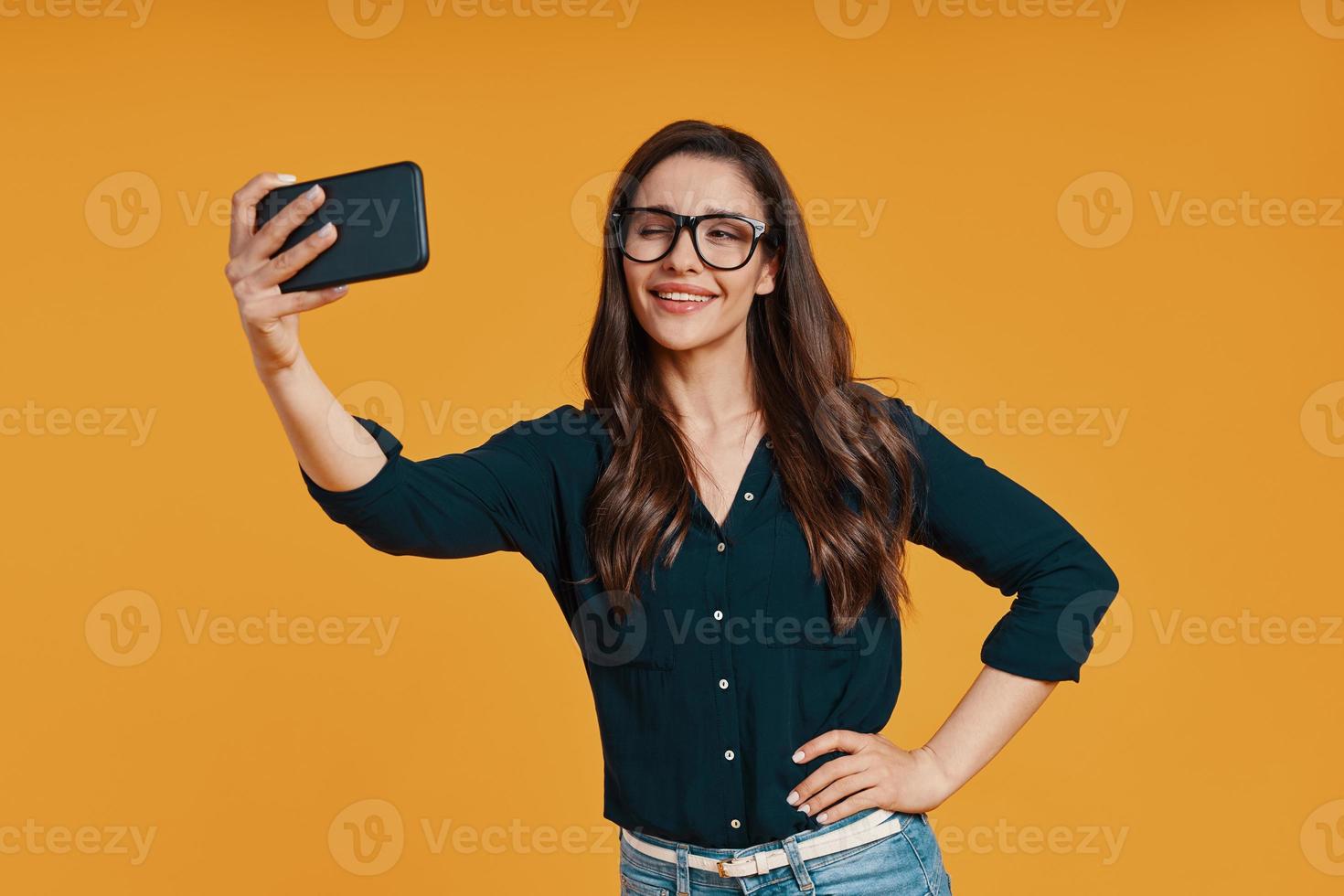 mujer joven feliz en ropa casual tomando selfie y guiñando un ojo foto
