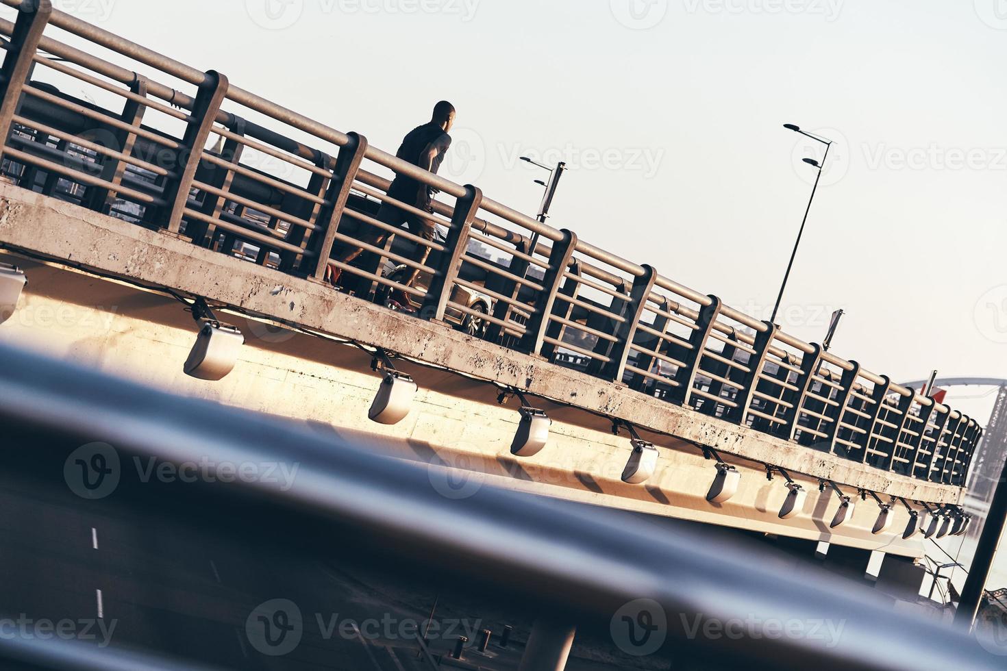 llena de energía. joven africano con ropa deportiva haciendo ejercicio mientras trotaba en el puente al aire libre foto