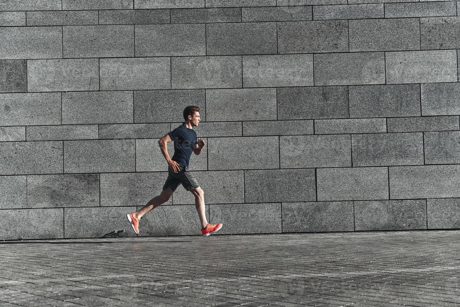 Faster than ever. Full length of young man in sports clothing running while exercising outside photo