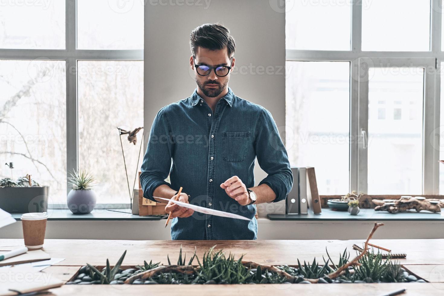 Inspired to work hard. Thoughtful young man working with correspondence while standing in the office photo