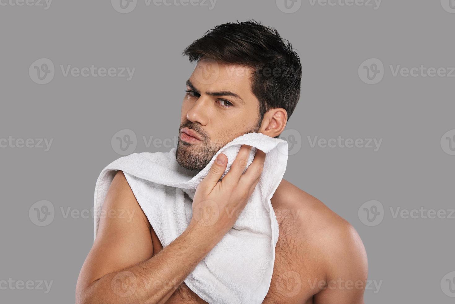 Everyday routine. Handsome young man wiping his face with towel while