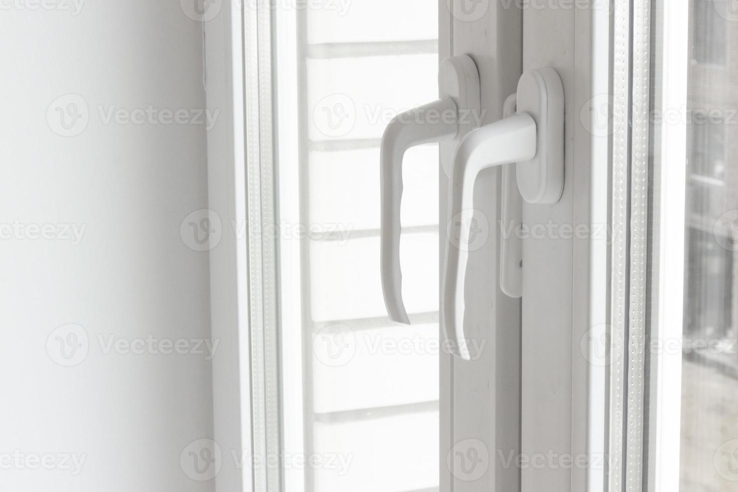 White plastic window handles detail, closeup view, horizontal photo. Closed modern windows in flat, PVC plastic, handles turned down side view, cold weather photo