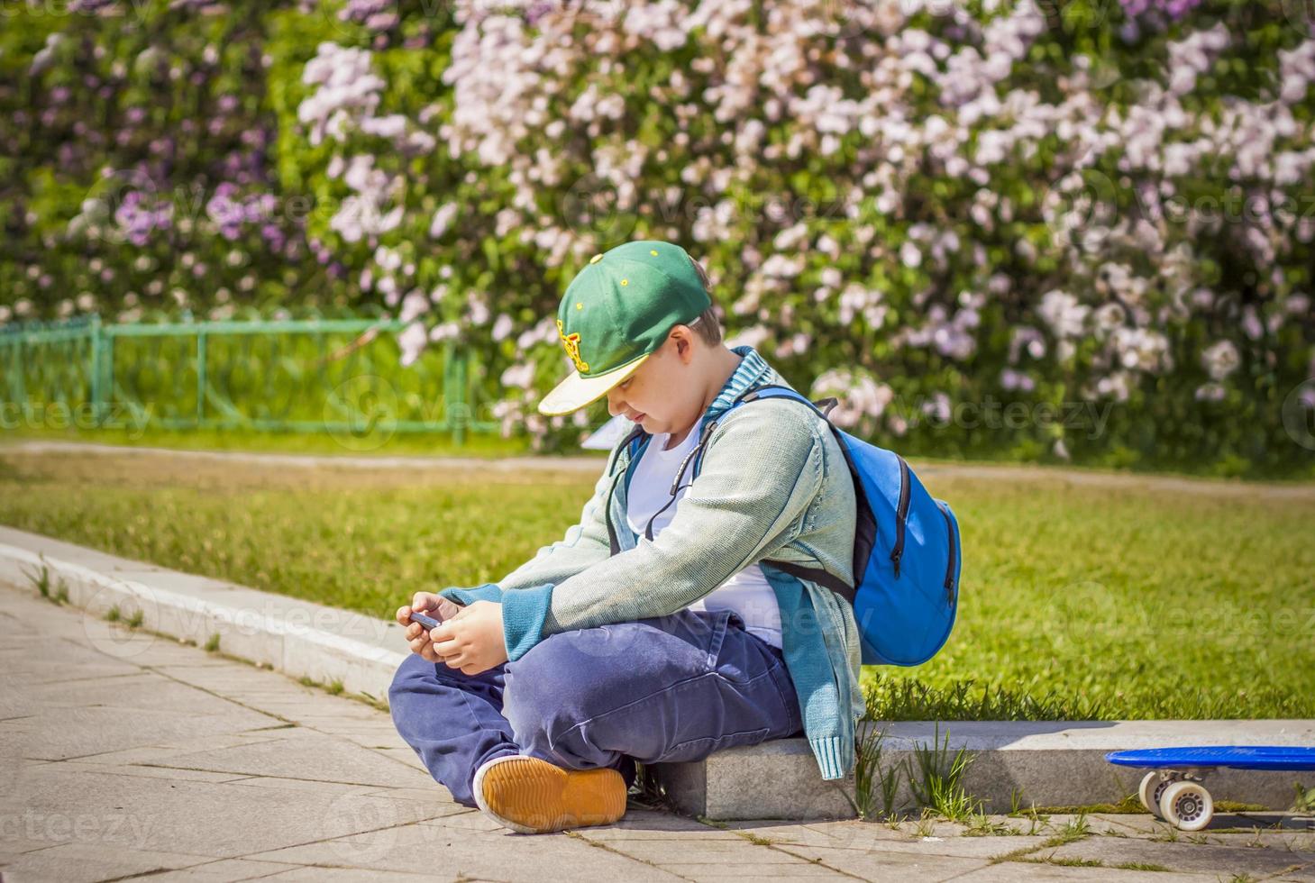 un joven está sentado al lado de un callejón lila y mira su teléfono. contra el fondo de arbustos de lilas. interacciones. enfoque selectivo. foto