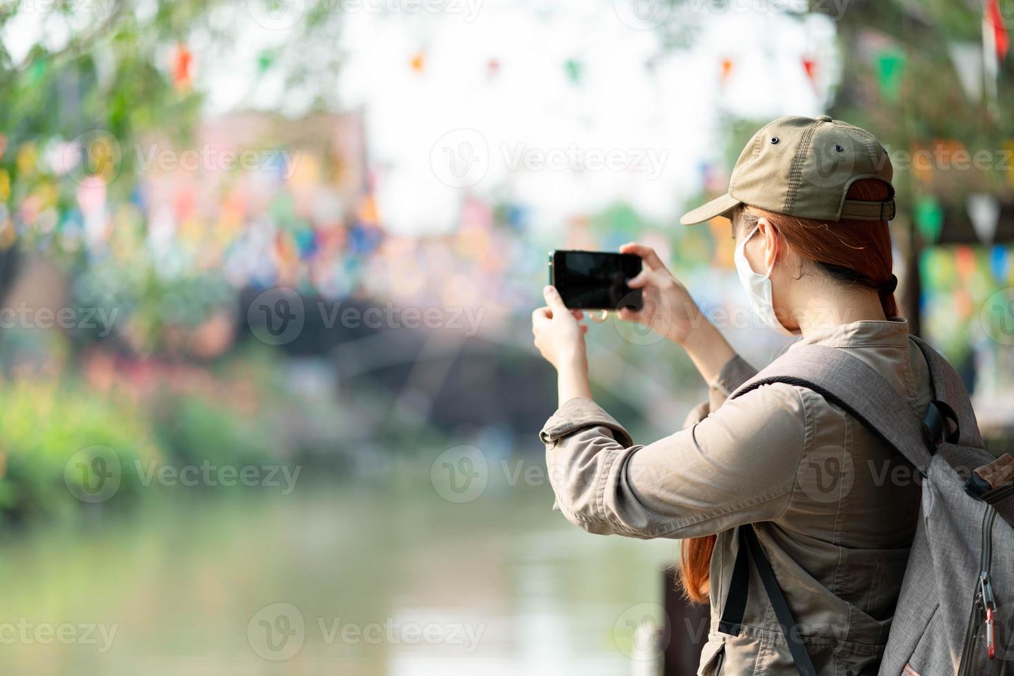 Young asian traveller with hat, backpack and mask taking photo while solo travel in ayutthaya thailand