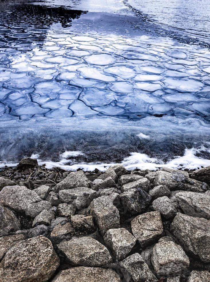 winter landscape of freezing lake shore , the first frosts on the lake in the form of small ice cubes and large stones on the shore snow and ice photo