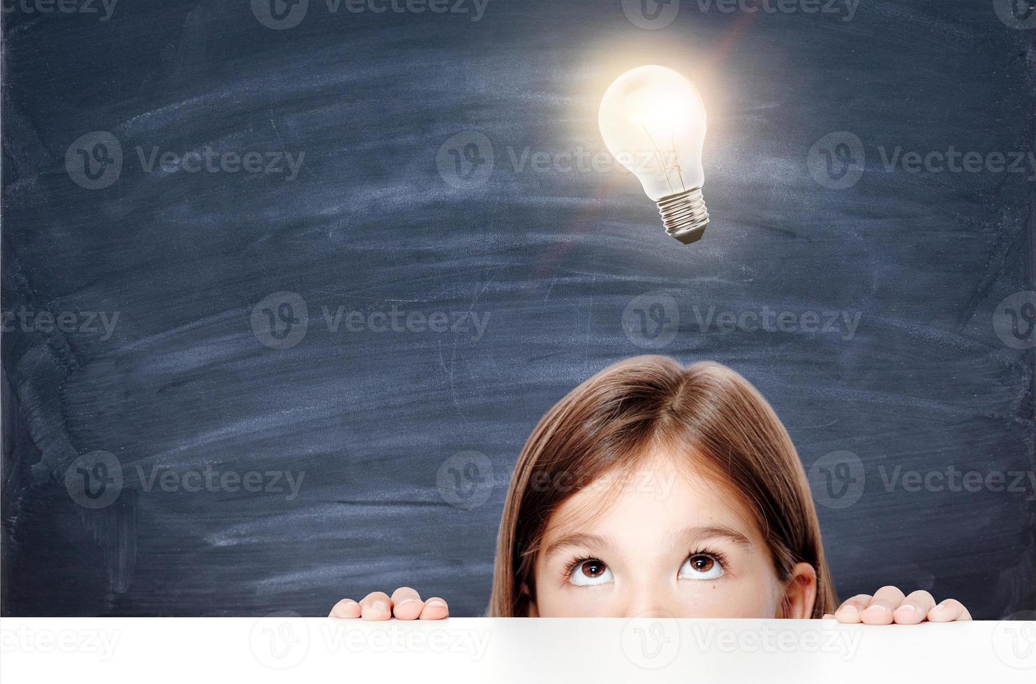 Young cute girl at chalkboard with light bulb over head photo