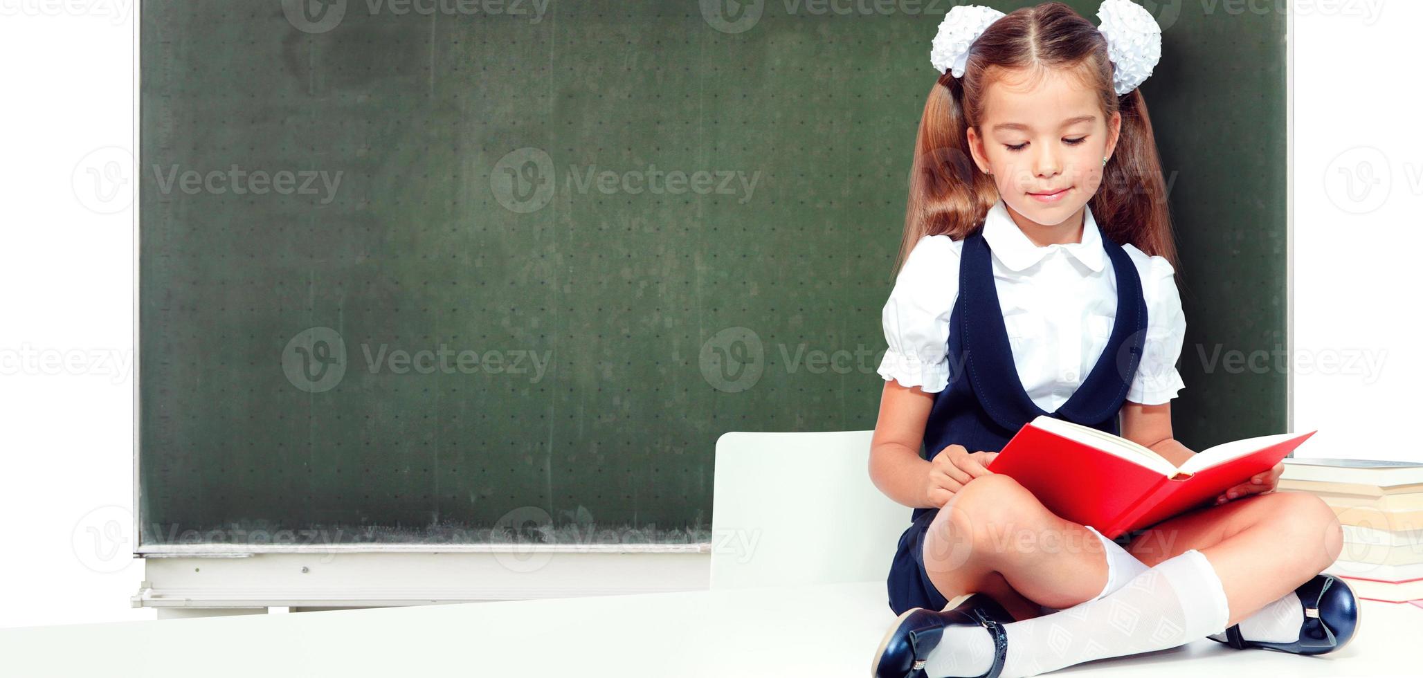 Young cute girl sitting at the table and reading a book photo