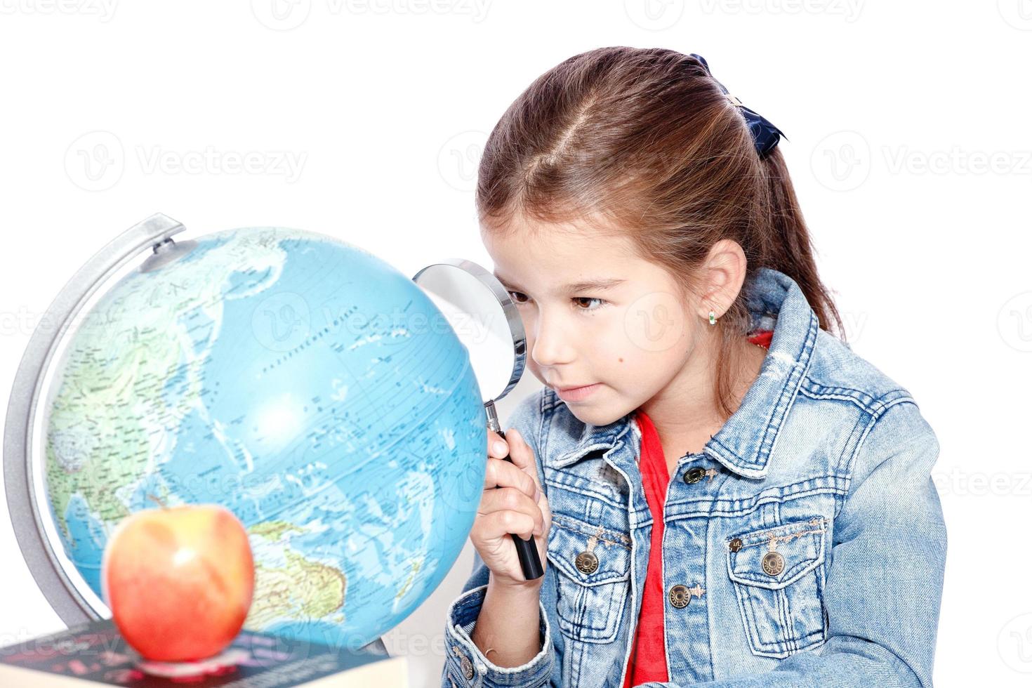 Curious little girl looking through magnifying glass on globe photo