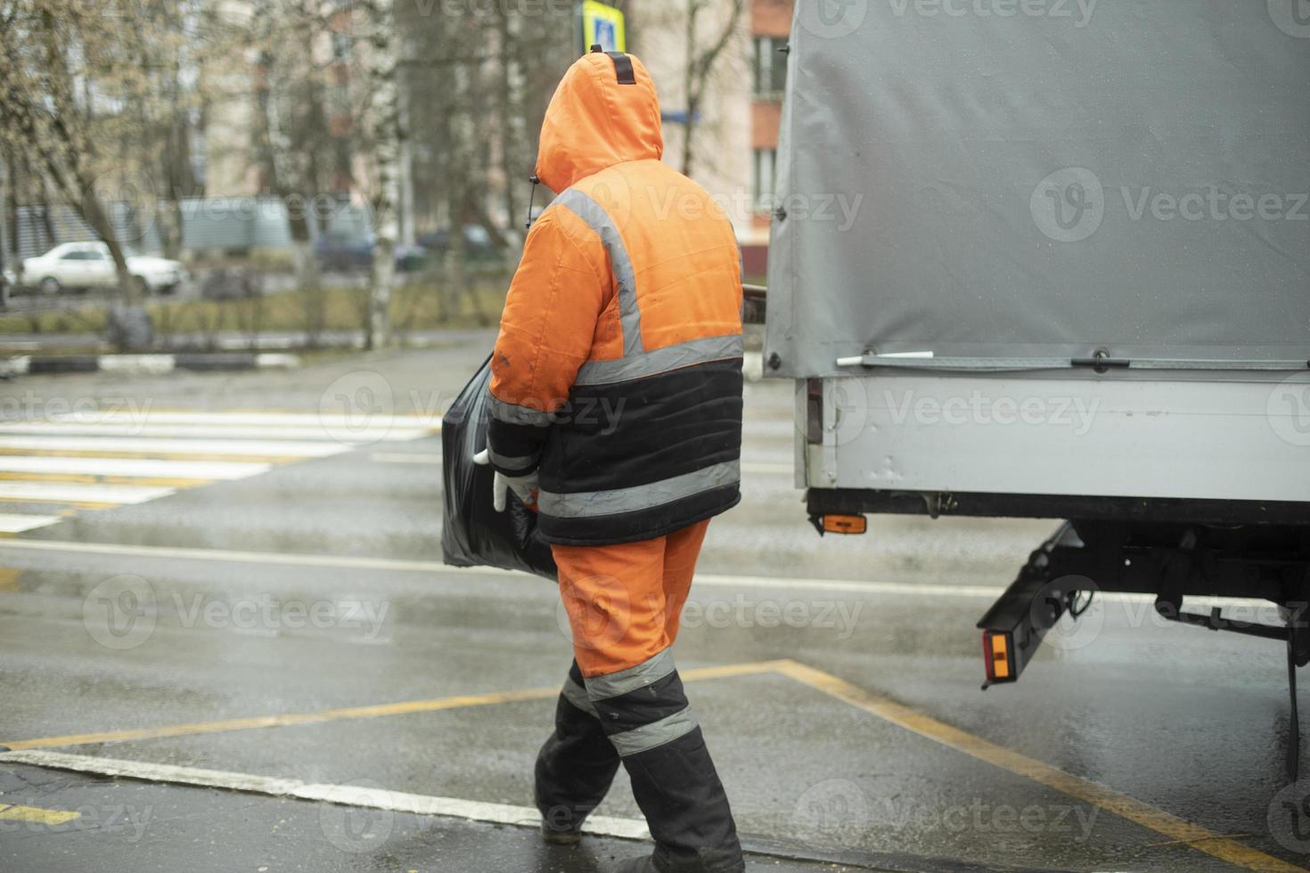 Worker puts cargo in transport. Orange clothes for work. Cleaning road. photo