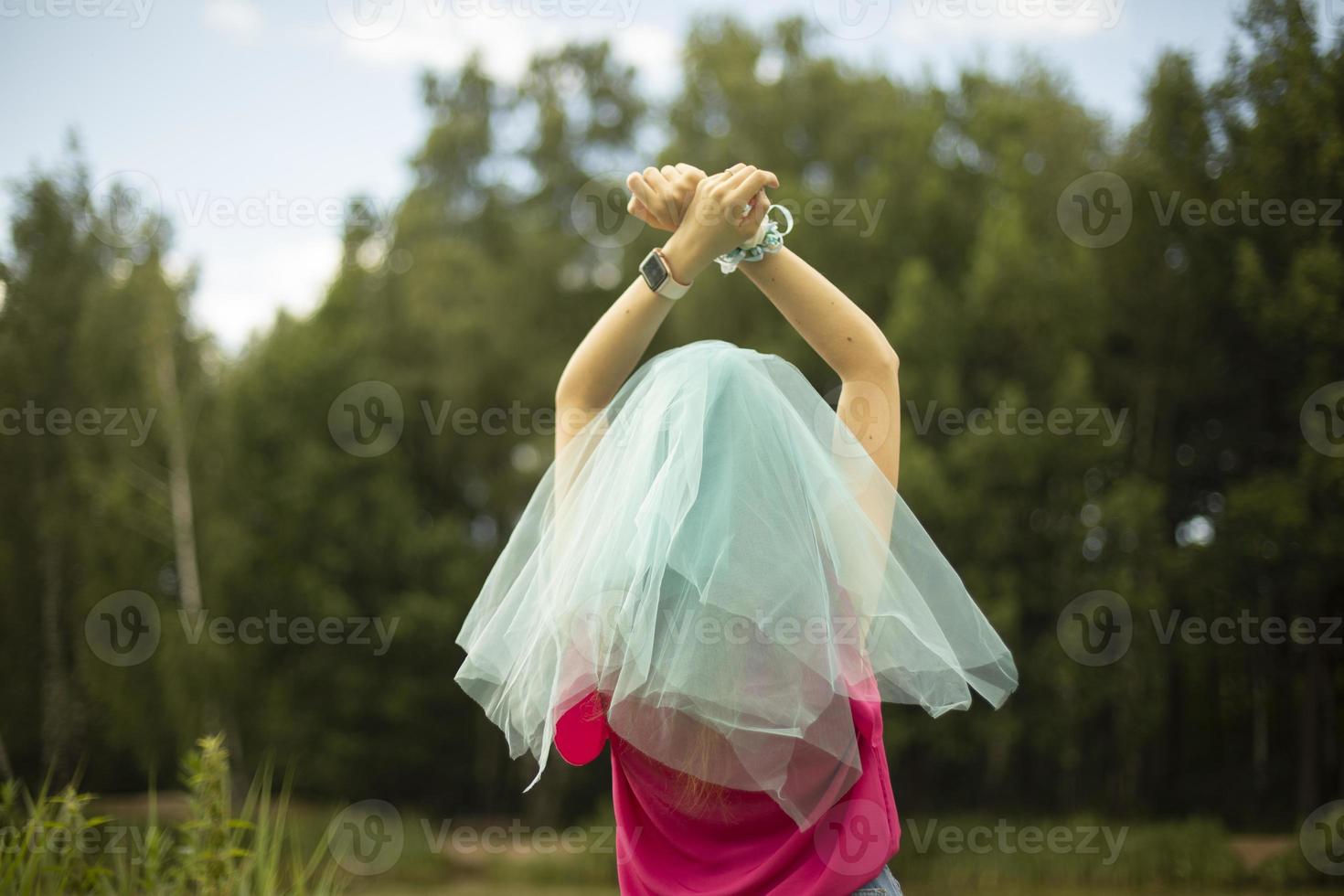 Blue veil on head. Bridesmaid's clothes. Lightweight fabric in summer. Girl in park. Hands raised up. photo