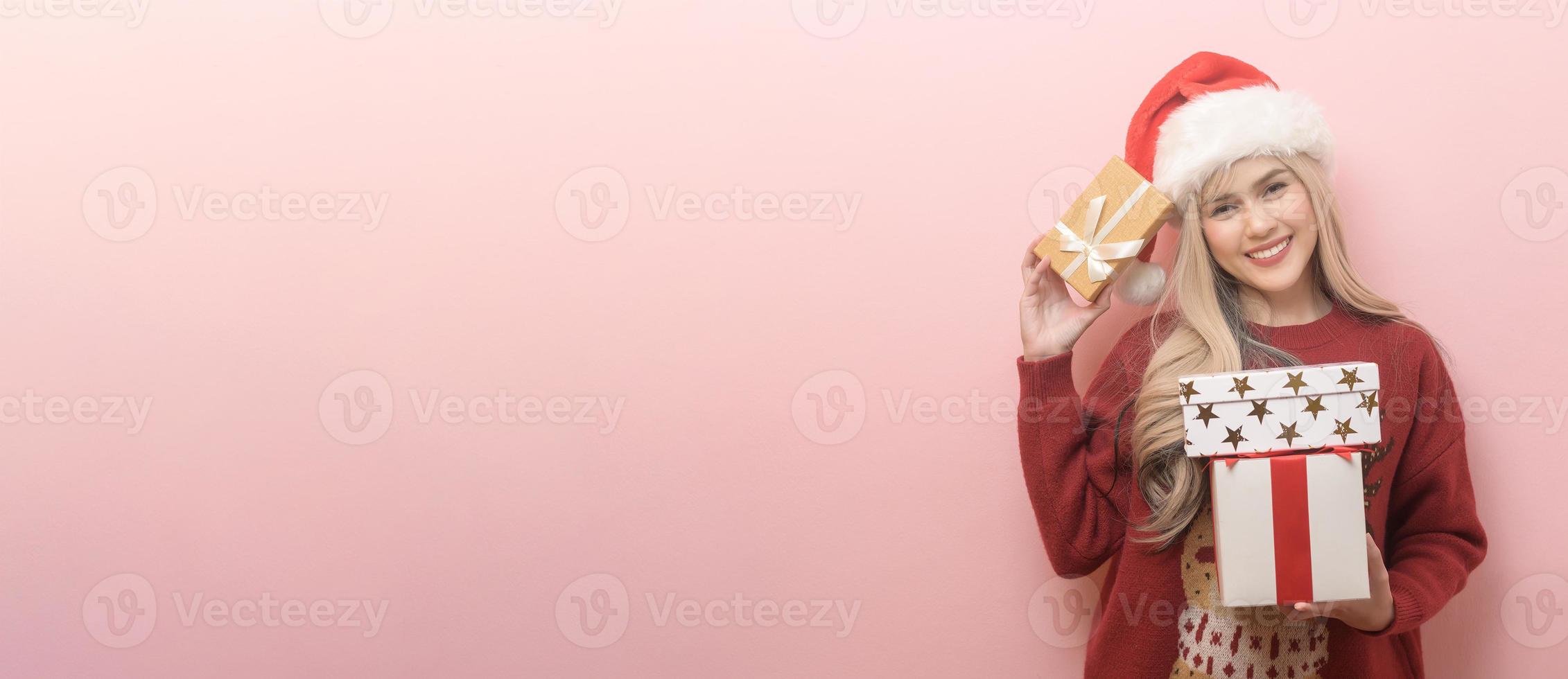 Portrait of happy Caucasian young woman in santa claus hat with gift box over pink background photo