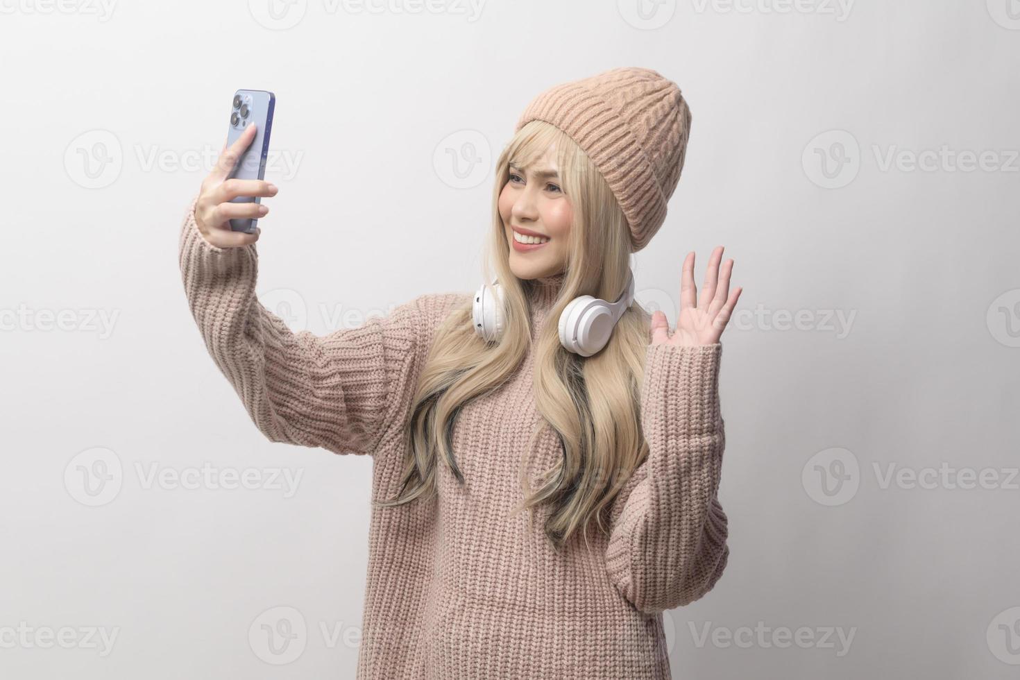 Portrait of Caucasian young woman wearing sweater holding smart phone   over white background photo