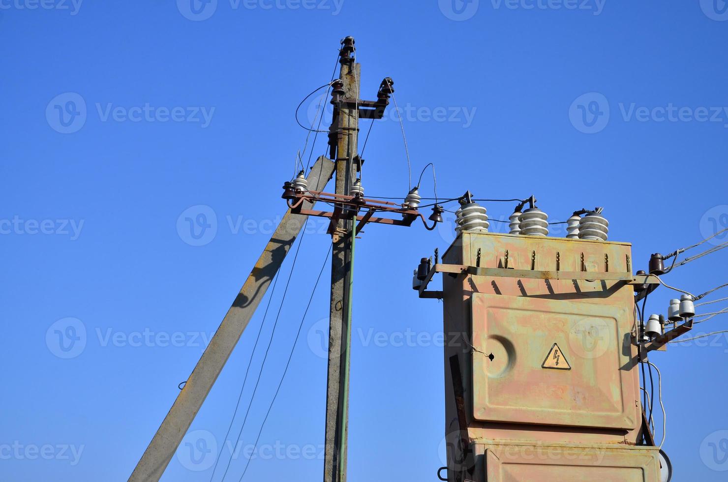 Old and obsolete electrical transformer against the background of a cloudless blue sky. Device for distribution of supply of high-voltage energy photo