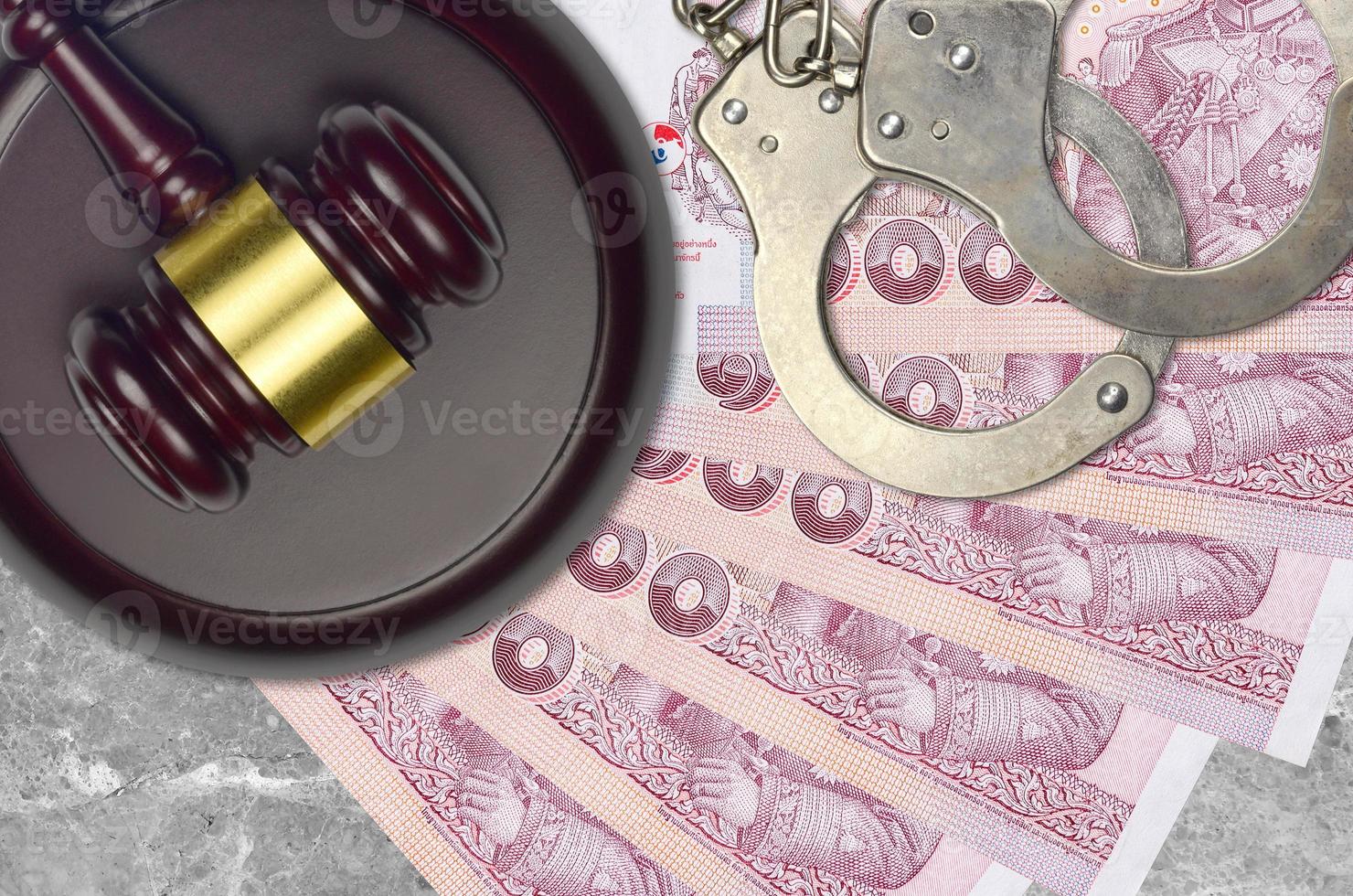 100 Thai Baht bills and judge hammer with police handcuffs on court desk. Concept of judicial trial or bribery. Tax avoidance photo