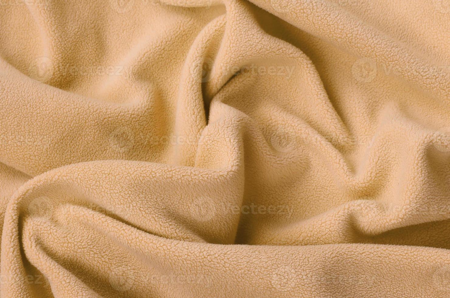 The blanket of furry orange fleece fabric. A background of light orange soft plush fleece material with a lot of relief folds photo