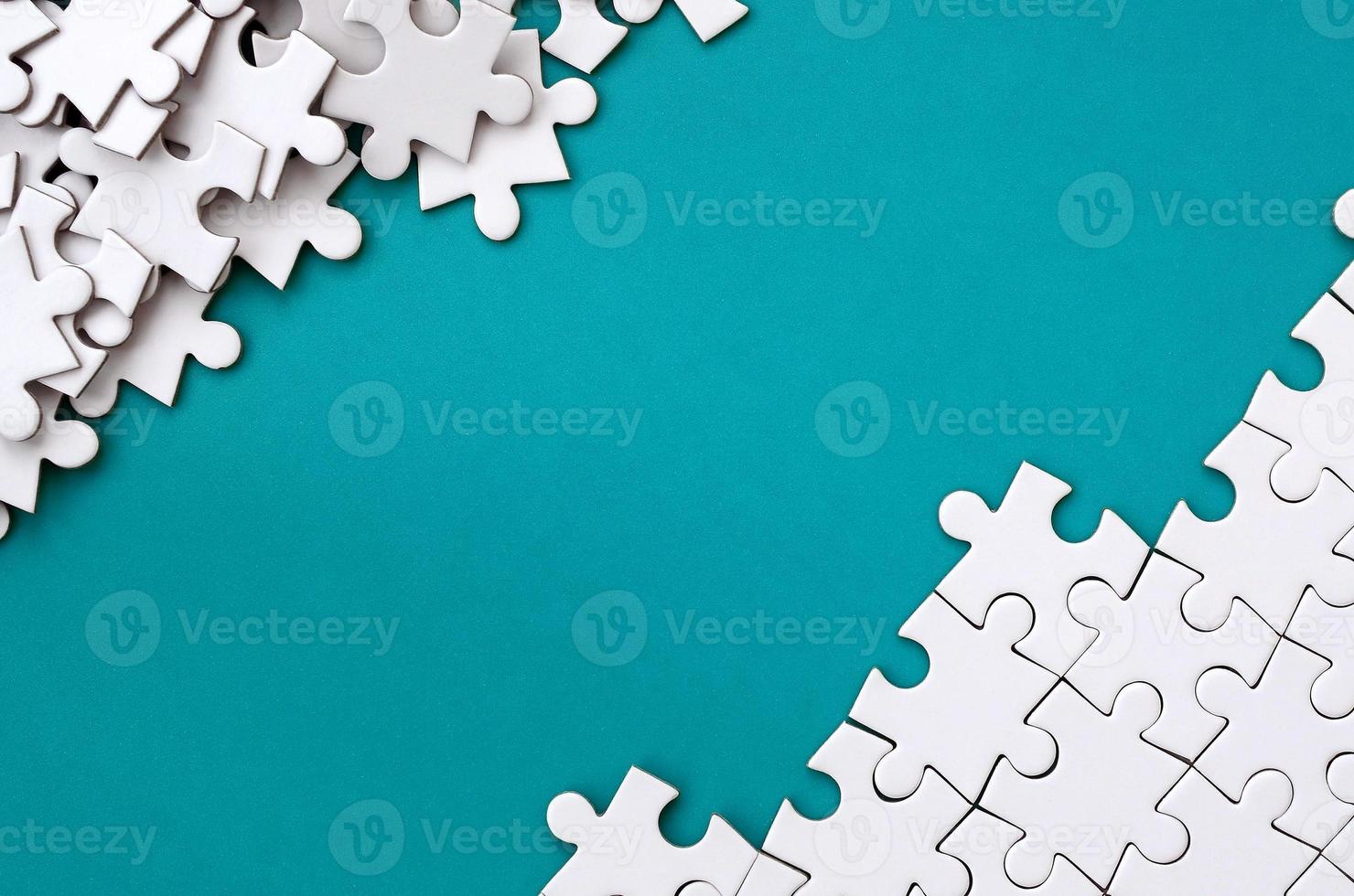 Fragment of a folded white jigsaw puzzle and a pile of uncombed puzzle elements against the background of a blue surface. Texture photo with space for text