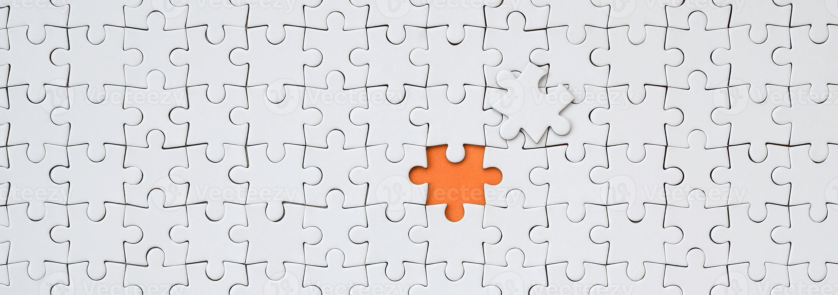 The texture of a white jigsaw puzzle in an assembled state with one missing element forming an orange space photo
