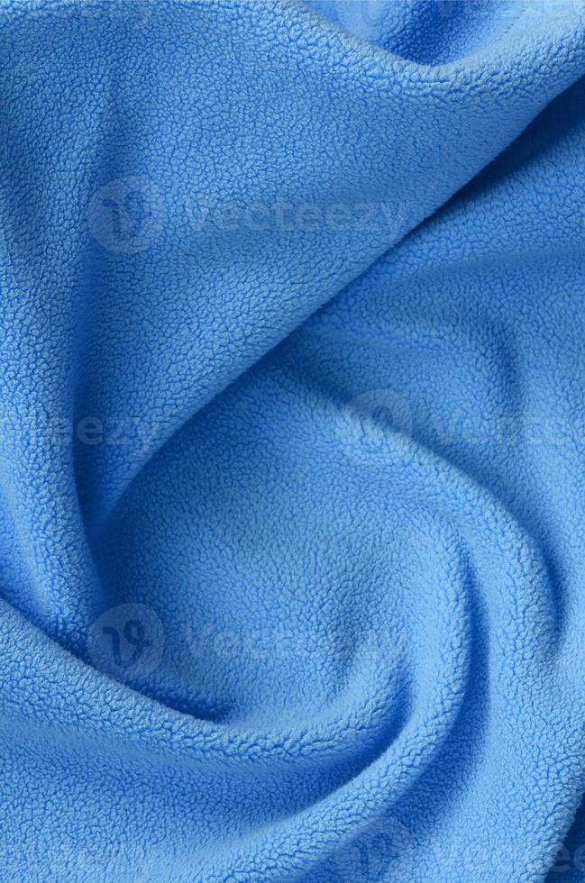 The blanket of furry blue fleece fabric. A background of light blue soft plush fleece material with a lot of relief folds photo