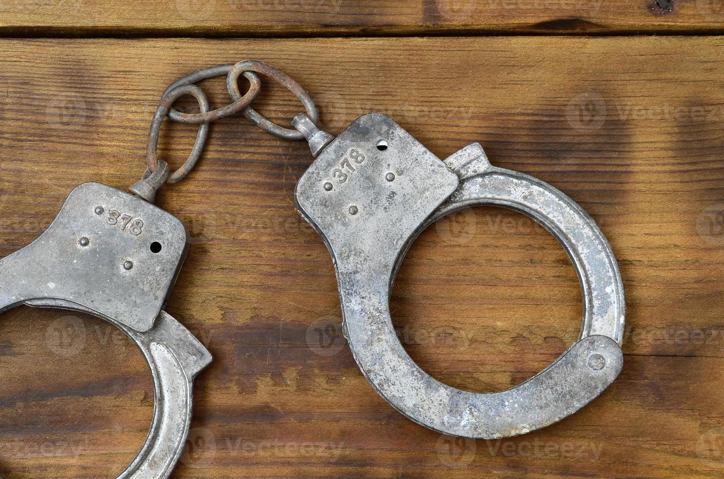 Old and rusty police handcuffs lie on a scratched wooden surface. The concept of an old crime photo