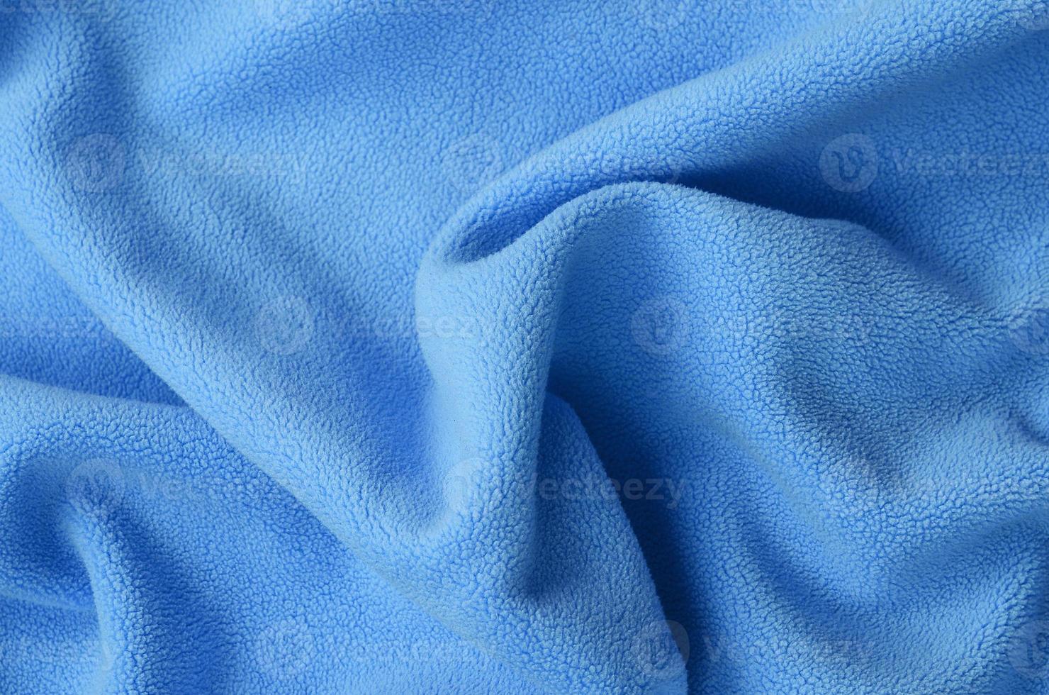 The blanket of furry blue fleece fabric. A background of light blue soft plush fleece material with a lot of relief folds photo
