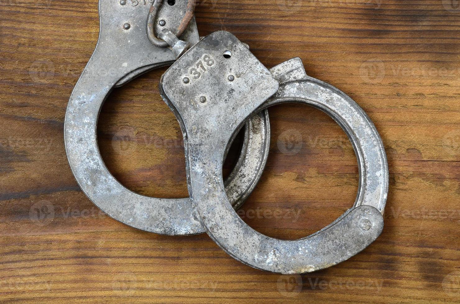 Old and rusty police handcuffs lie on a scratched wooden surface. The concept of an old crime photo