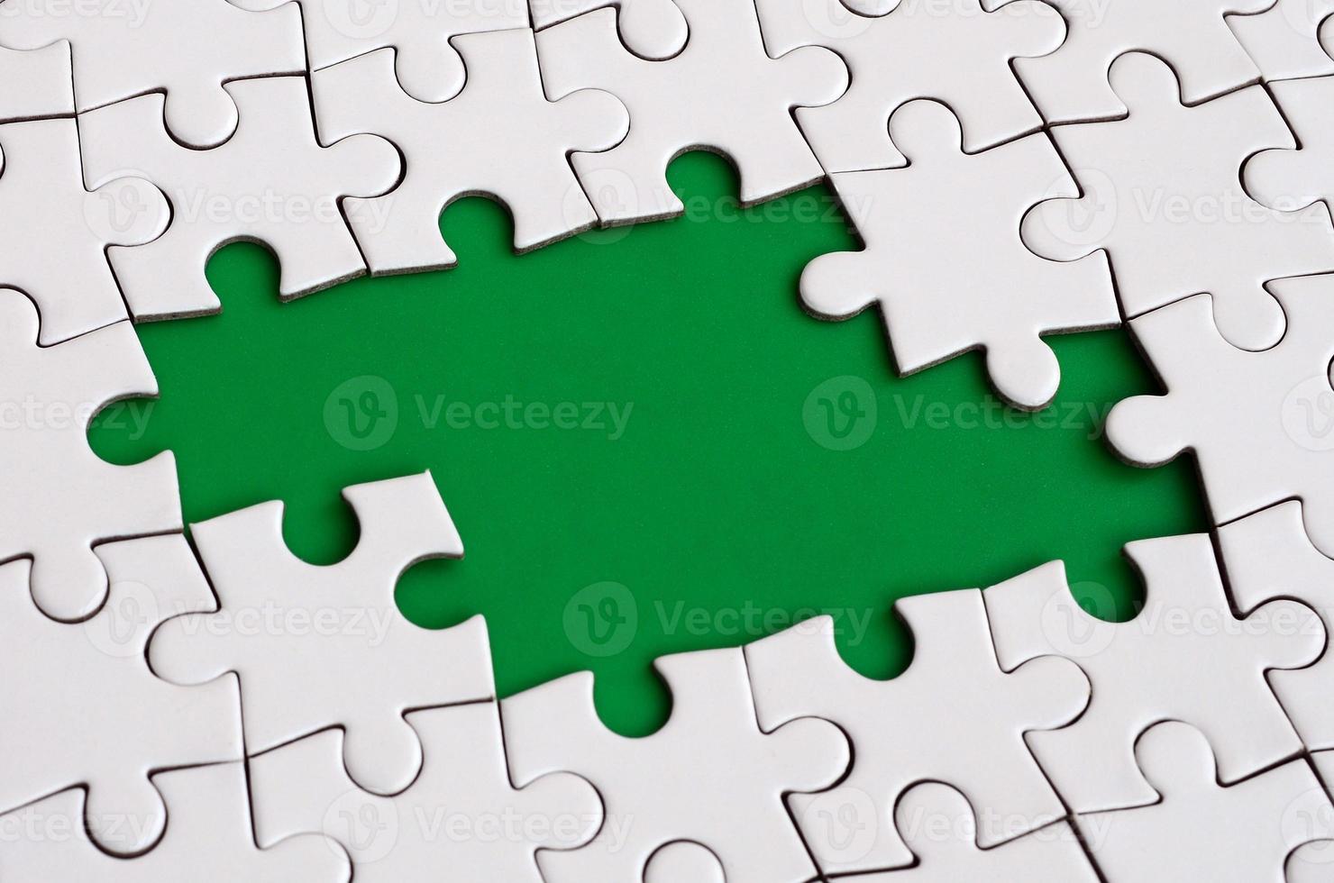 Close-up texture of a white jigsaw puzzle in assembled state with missing elements forming a green pad for text. Copy space photo