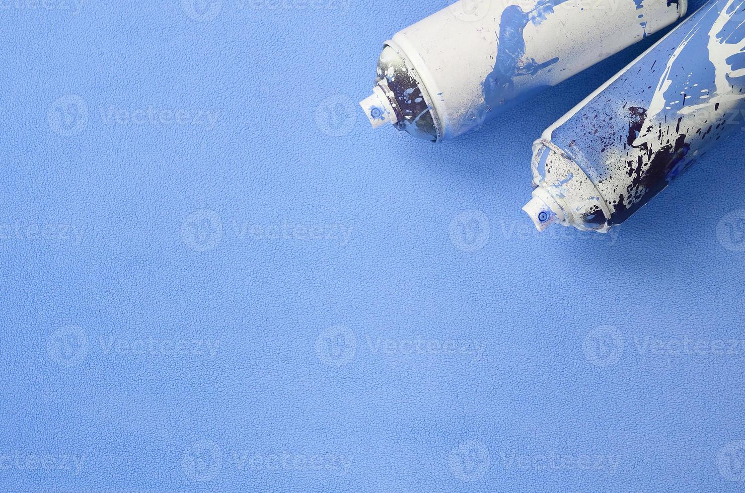 Some used blue aerosol spray cans with paint drips lies on a blanket of soft and furry light blue fleece fabric. Classic female design color. Graffiti hooliganism concept photo