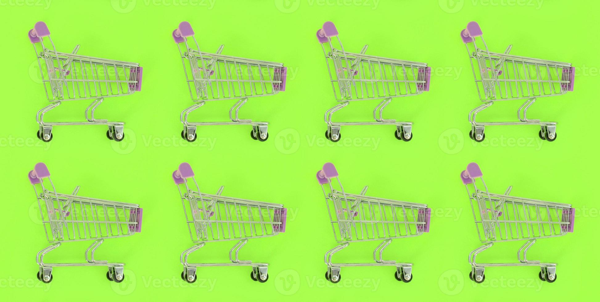 Shopping addiction, shopping lover or shopaholic concept. Many small empty shopping carts perform a pattern on a pastel colored paper background. Flat lay composition, top view photo
