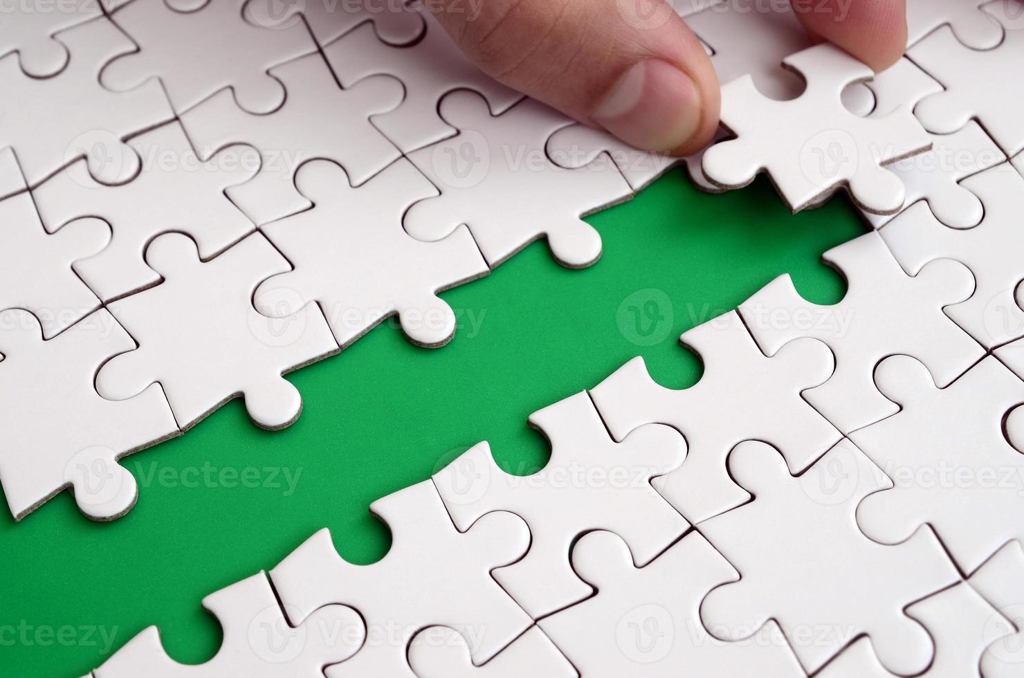 The human hand paves the way to the surface of the jigsaw puzzle, forming a green space. The concept of overcoming the difficulties on the way to success photo
