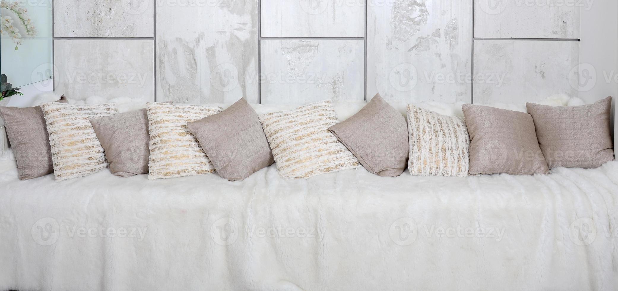 Many pillows lie on the couch, which is covered with a large plush veil against the background