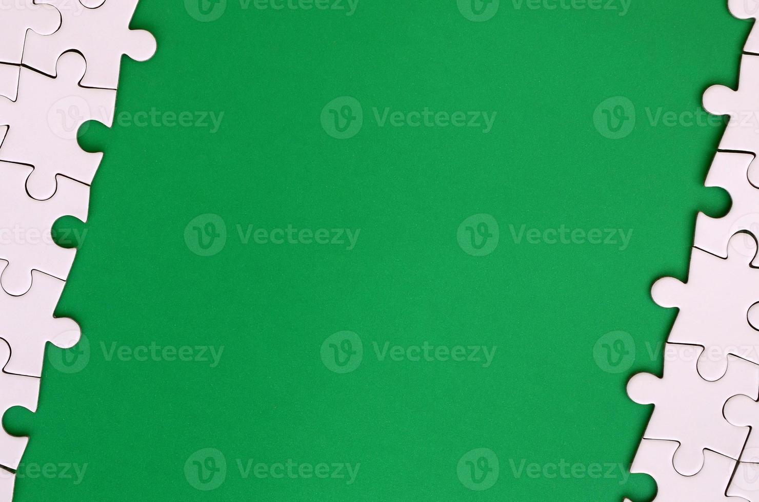 Fragment of a folded white jigsaw puzzle on the background of a green plastic surface. Texture photo with copy space for text