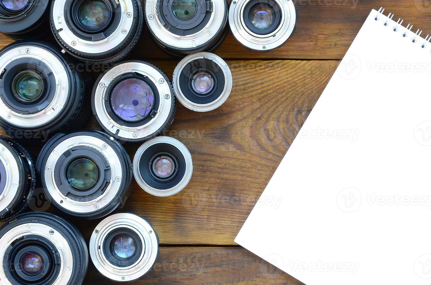 Several photographic lenses and white notebook lie on a brown wooden background. Space for text photo
