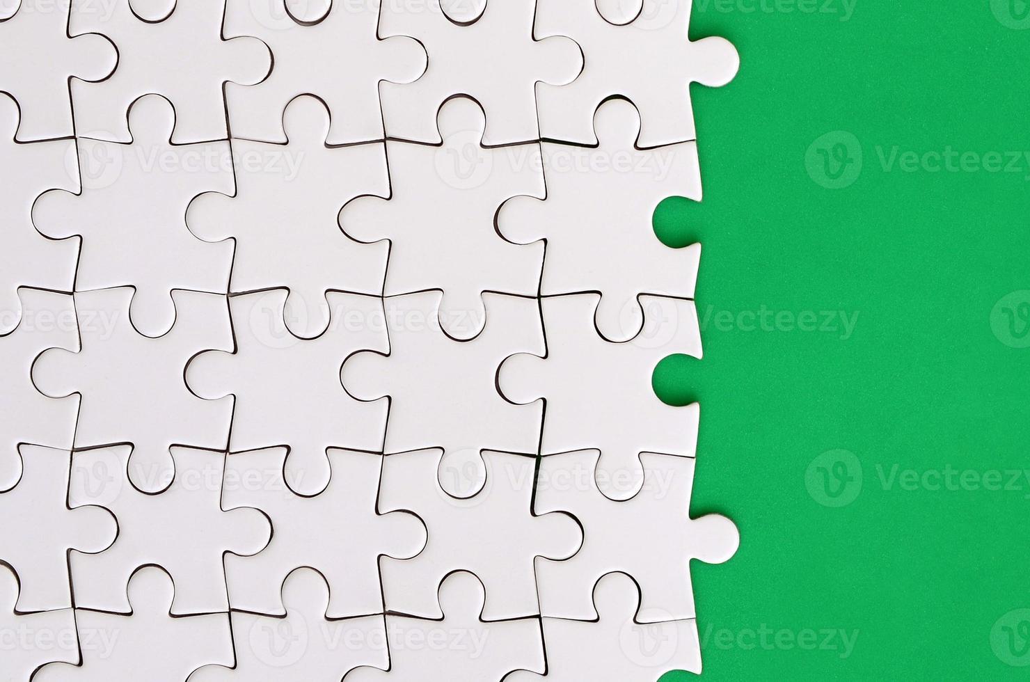 Fragment of a folded white jigsaw puzzle on the background of a green plastic surface. Texture photo with copy space for text