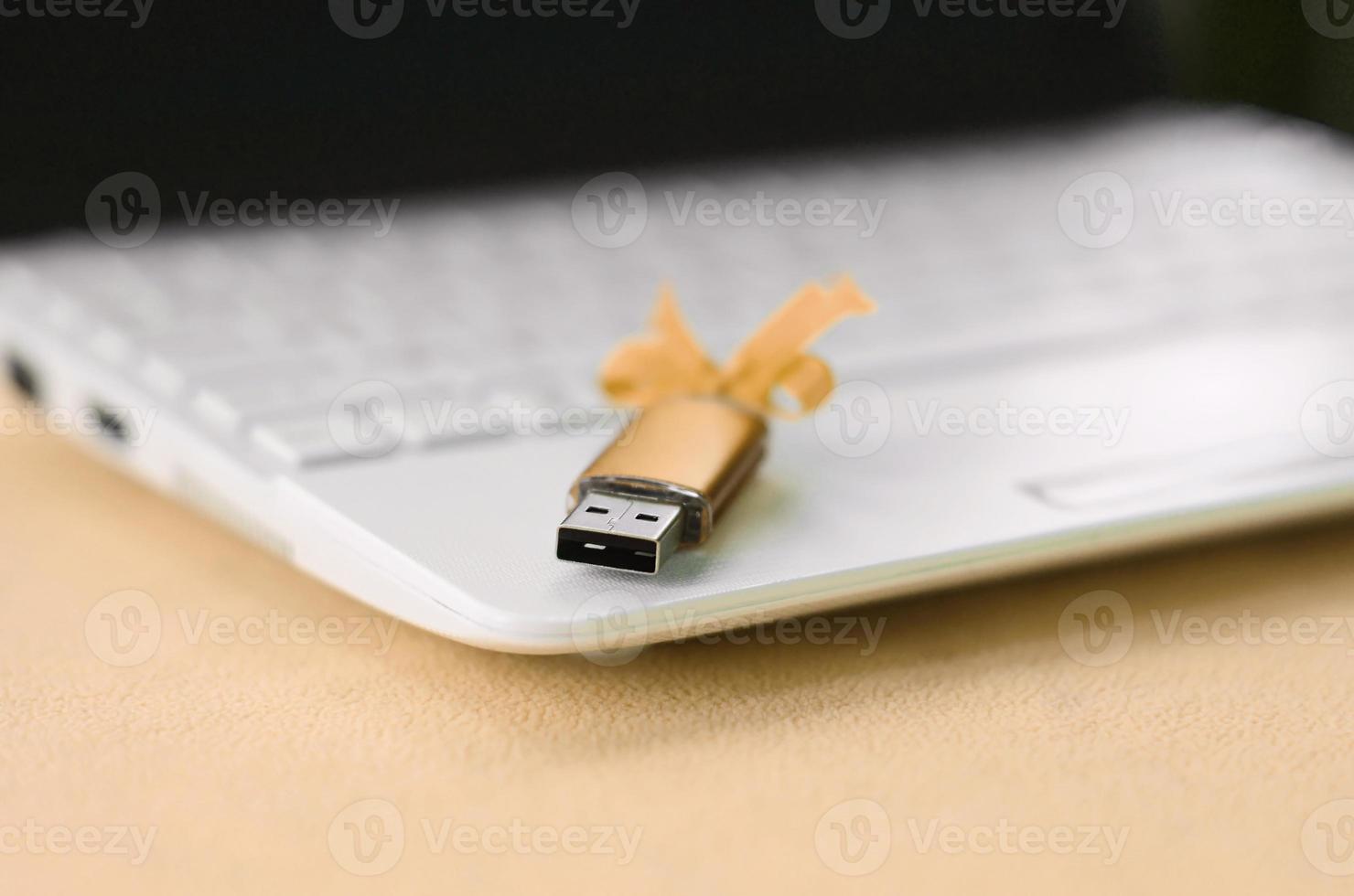 Orange usb flash memory card with a bow lies on a blanket of soft and furry light orange fleece fabric beside to a white laptop. Classic female gift design for a memory card photo