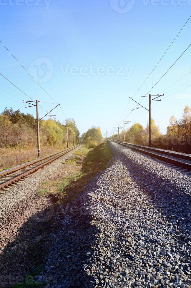 Autumn industrial landscape. Railway receding into the distance among green and yellow autumn trees photo